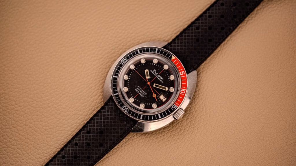 A vintage black and red dive watch with a textured black strap rests on a beige leather surface—an ideal piece for any vintage watch enthusiast or those seeking inspiration from a watch buying guide.