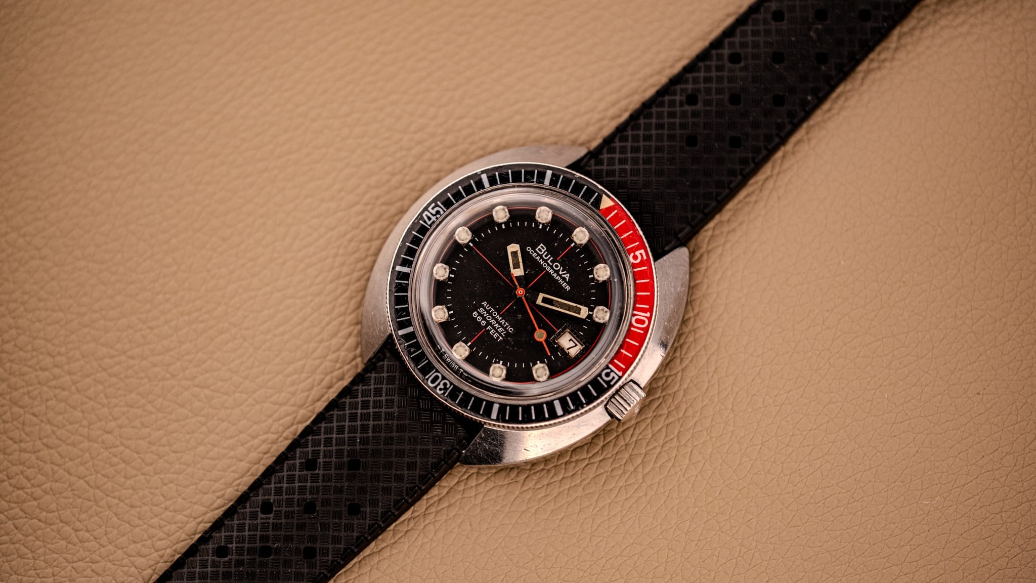 A vintage black and red dive watch with a textured black strap rests on a beige leather surface—an ideal piece for any vintage watch enthusiast or those seeking inspiration from a watch buying guide.