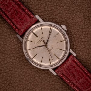 A Universal Geneve Polerouter 20375-4 "Incognito Dial" with a Micro Rotor Cal. 215 movement and a red leather strap rests on a brown textured surface.