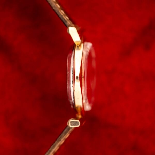 Side view of a Wittnauer Automatic Ref. 2598-2 with an Asymmetric Case (Cal. 11AO) and brown leather strap, showcased against a vibrant red background.