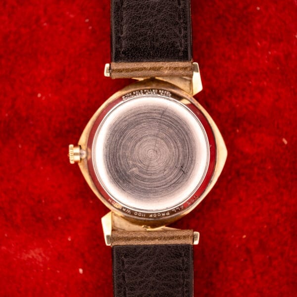 Close-up of the back of a Wittnauer Automatic Ref. 2598-2 Asymmetric Case Cal. 11AO wristwatch with a black leather strap, resting on a red textured surface.