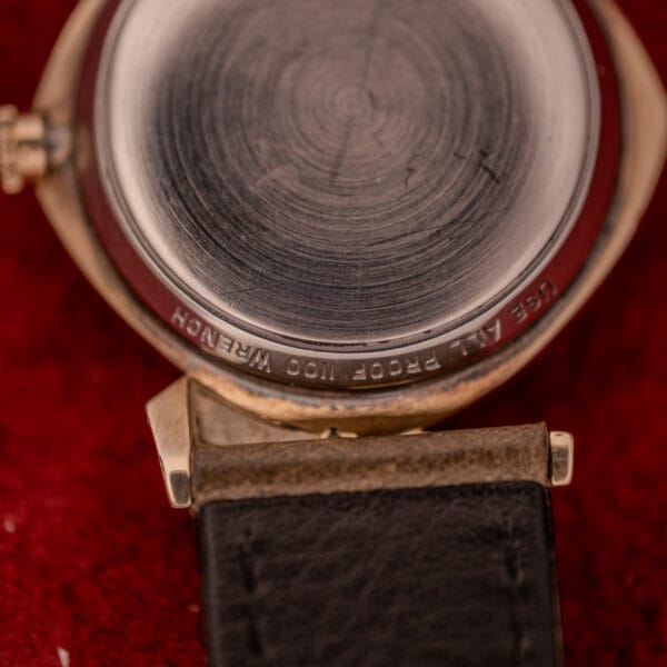 Close-up of the Wittnauer Automatic Ref. 2598-2 with asymmetric case and leather strap, featuring Cal. 11AO movement, resting on a red textured surface.