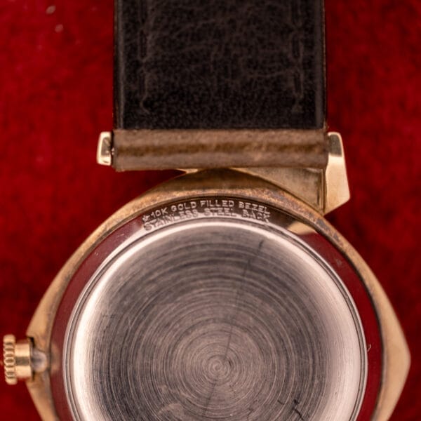 Close-up of the back of a Wittnauer Automatic Ref. 2598-2 with Asymmetric Case Cal. 11AO and leather strap, set on a red surface.