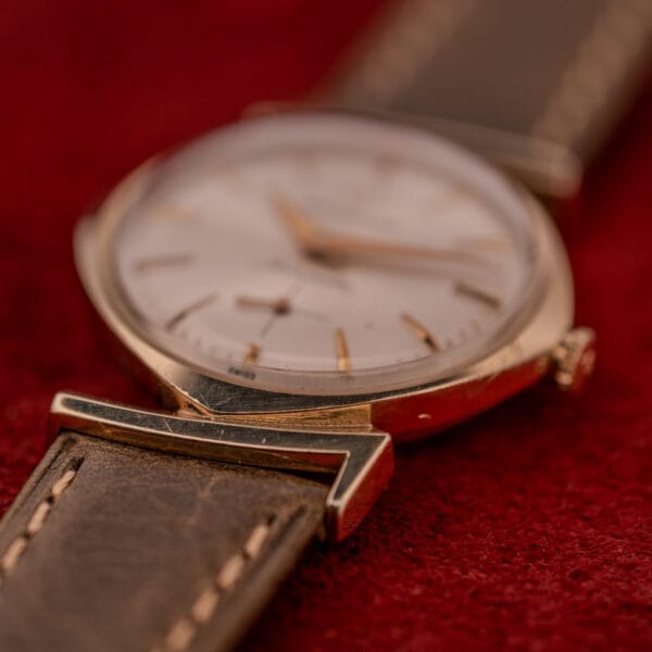 Close-up of a Wittnauer Automatic Ref. 2598-2 with an asymmetric case and brown leather strap, featuring Cal. 11AO, displayed on a red textured surface.