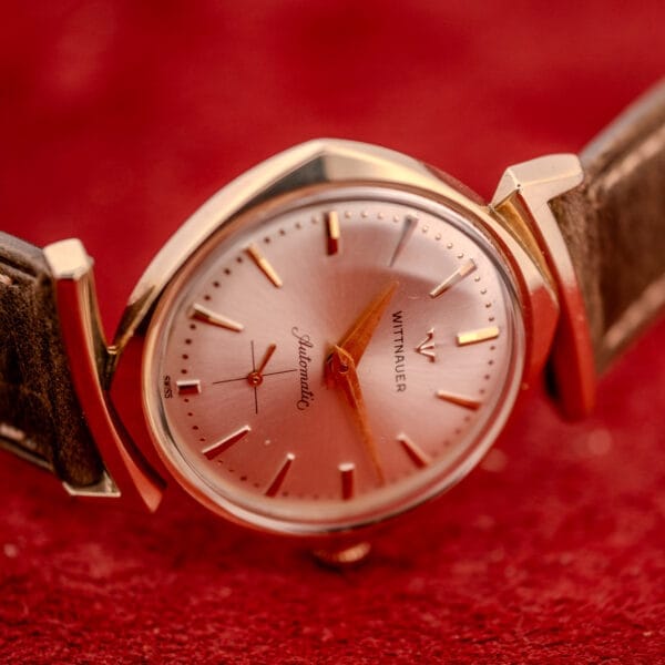 A Wittnauer Automatic Ref. 2598-2 with an Asymmetric Case (Cal. 11AO) and leather strap, displayed on a red textured surface.