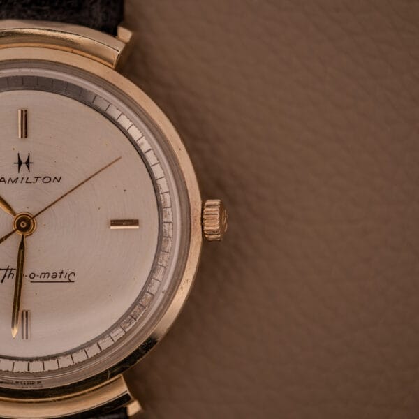 Close-up of a vintage Hamilton Thin-O-Matic Ref. T-406 with hooded lugs, gold case, leather strap, and Micro Rotor Cal. 663 movement.
