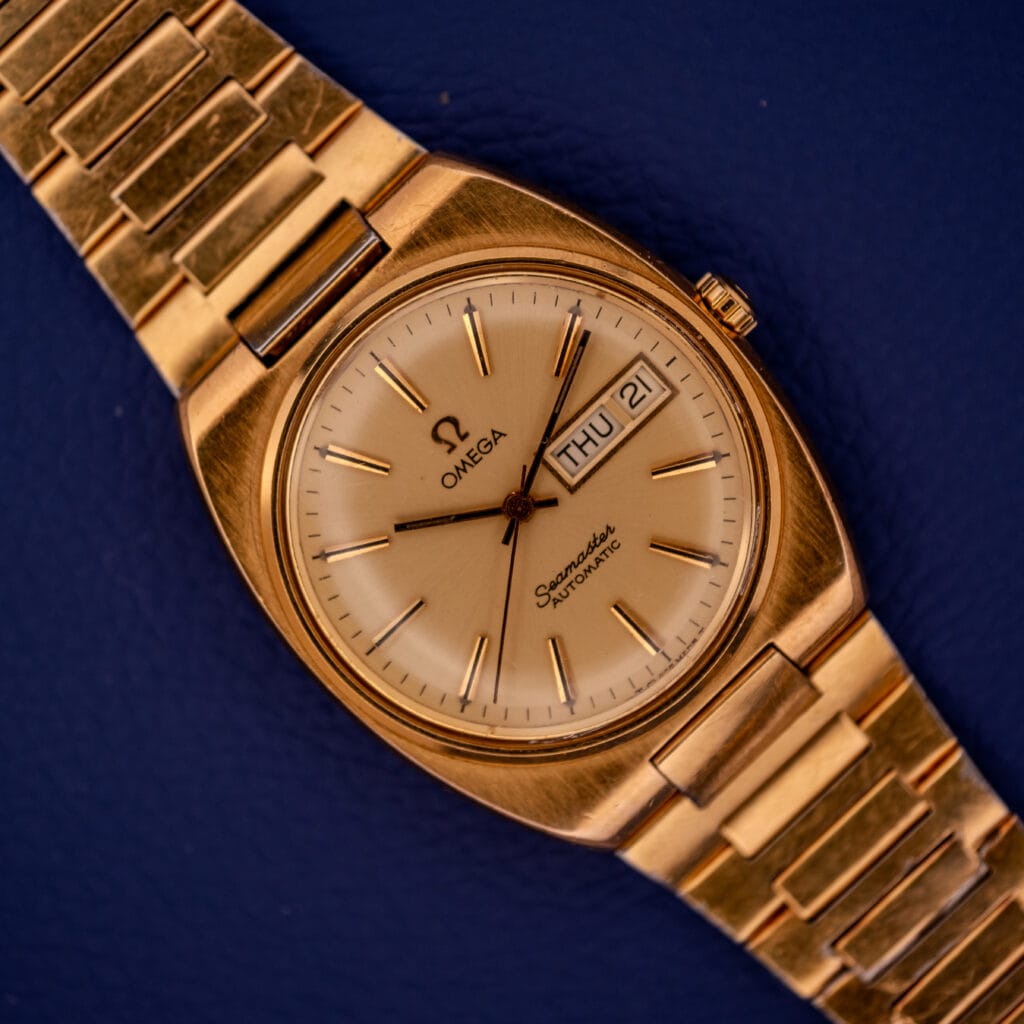 Omega Seamaster Automatic Day/Date 166.0216 Cal. 1022 watch in gold, shown on a blue background.
