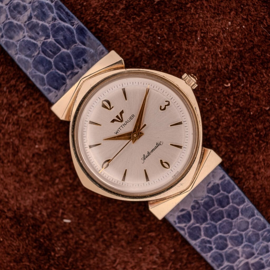 Wittnauer Automatic Ref. 2598-1 Hooded Lugs Cal. 11SR wristwatch with a blue textured band, shown on a brown background.