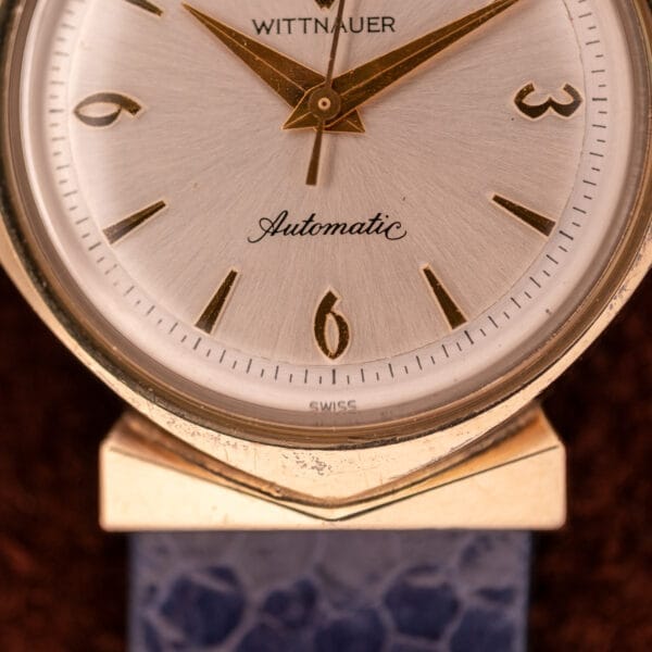 Close-up of a Wittnauer Automatic Ref. 2598-1 Hooded Lugs Cal. 11SR watch featuring gold hands, gold numbers, and a blue textured strap.