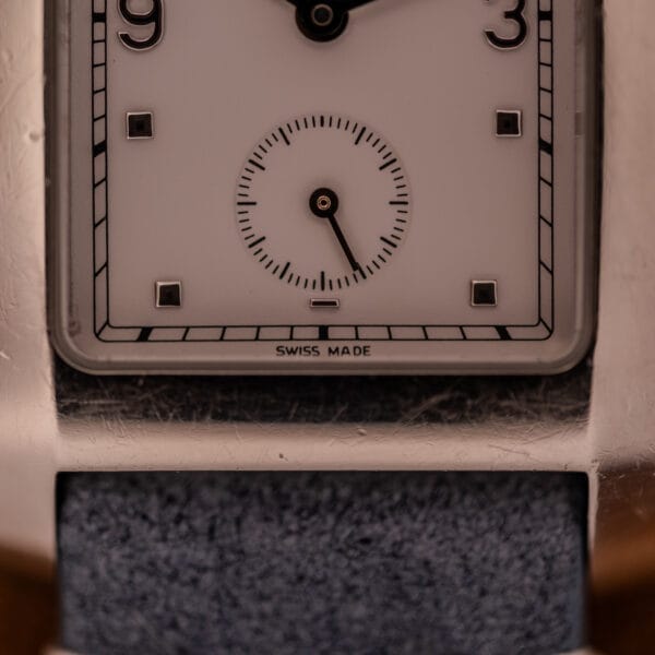Close-up of the Baume Mercier Hampton Large MV05063 watch's square white dial with black numerals, subdial, and a blue strap visible.