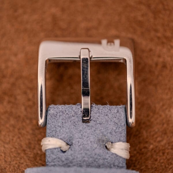 A close-up of the Baume Mercier Hampton Large MV05063’s silver buckle on a pale blue suede strap with white stitching, showcasing the refined style of this white dial quartz timepiece.