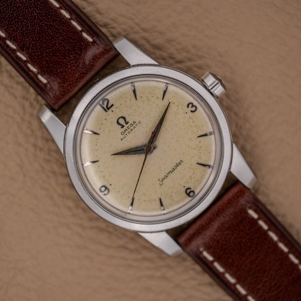 An Omega Automatic Seamaster Ref. 2846-2848 in stainless steel with a cream dial and brown leather strap rests elegantly on a tan surface.