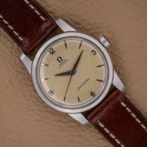 An Omega Automatic Seamaster Ref. 2846-2848 in stainless steel with a cream dial and brown leather strap rests elegantly on a tan surface.