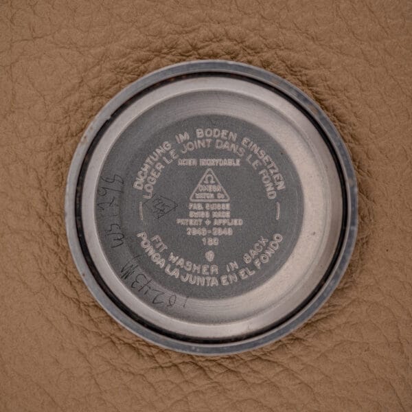 A close-up of an Omega Automatic Seamaster Ref. 2846-2848 Stainless Steel Cal. 500 watch case back, displaying the Cal. 500 markings, technical engravings, and multilingual instructions on a brown textured surface.