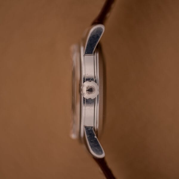 Side view of an Omega Automatic Seamaster Ref. 2846-2848 stainless steel Cal. 500 wristwatch case with crown, against a brown background.