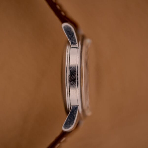 Side view of an Omega Automatic Seamaster Ref. 2846-2848 stainless steel wristwatch with a brown leather strap, displayed on a tan background.