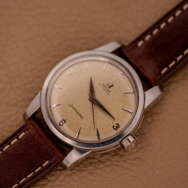 An Omega Automatic Seamaster Ref. 2846-2848 Stainless Steel Cal. 500 watch with a brown leather strap rests elegantly on a textured tan surface.