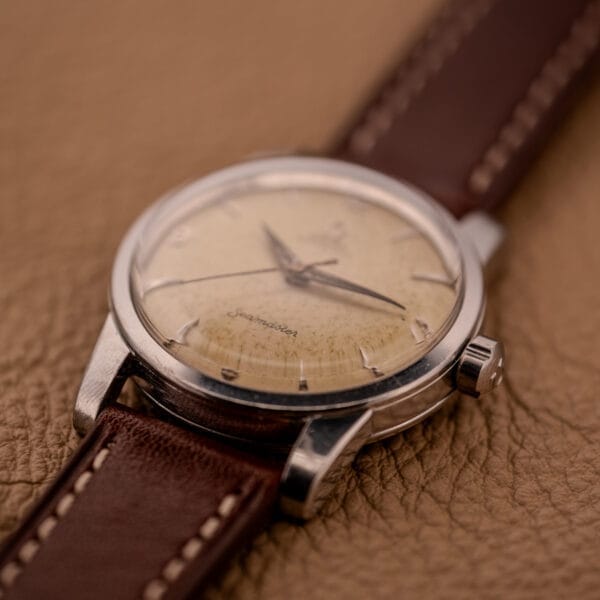 An Omega Automatic Seamaster Ref. 2846-2848 Stainless Steel Cal. 500 with a brown leather strap rests elegantly on a textured tan surface.