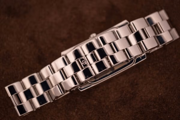 Baume Mercier Hampton MV045120 signed deployant clasp close-up, Phi emblem centered on polished steel cover, three-row bracelet flanking either side.