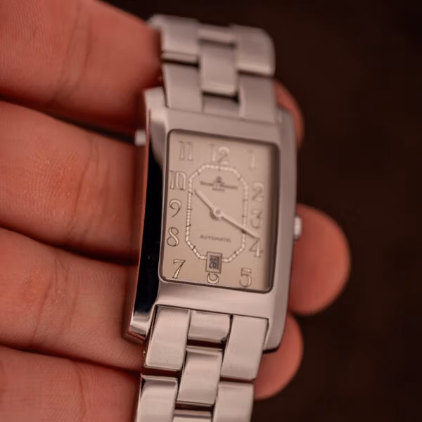 In-hand Baume Mercier Hampton Automatic MV045120 wrist shot showing rectangular case proportions, signed crown at three, champagne dial in indoor light.