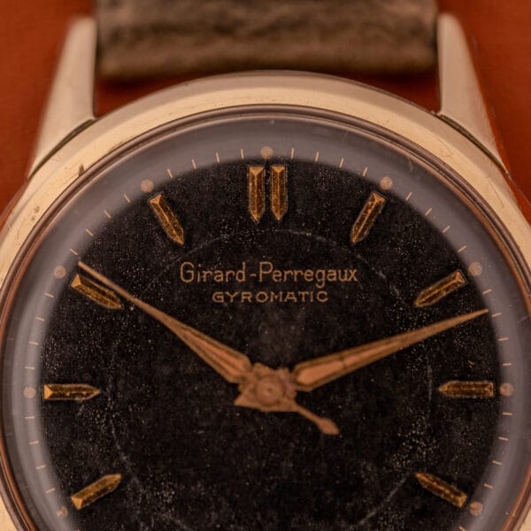 Close-up of a Girard Perregaux Gyromatic Ref. 6250, showcasing a black gilt dial with gold markers and a gold capped case.