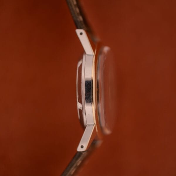 Side view of a Girard Perregaux Gyromatic Black Gilt Dial Ref. 6250 with gold capped case and brown leather strap against a brown background.