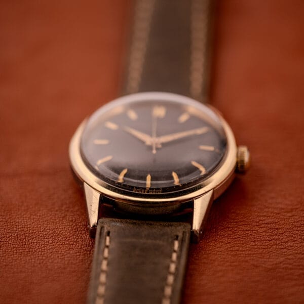 Girard Perregaux Gyromatic Black Gilt Dial Ref. 6250, Gold Capped Case wristwatch with a black leather strap displayed elegantly on a brown leather surface.