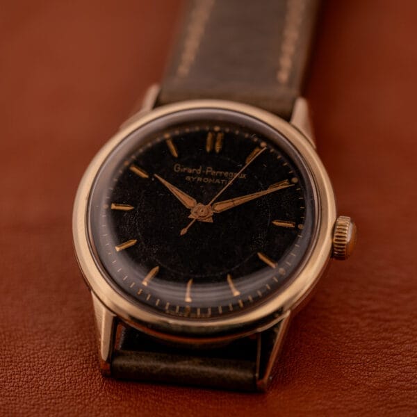 The Girard Perregaux Gyromatic Ref. 6250 features a black gilt dial, gold capped case, and brown leather strap for a classic vintage look.