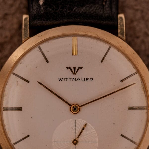 The Wittnauer Ref. 2028 features a manual wind Cal. 11BG2 movement, white dial with gold indexes, gold case, and black leather strap.