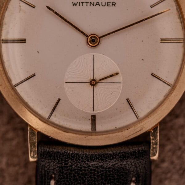 Close-up of a Wittnauer Ref. 2028 featuring a Manual Wind Cal. 11BG2, white dial with gold indexes and hands, set on a black leather strap.