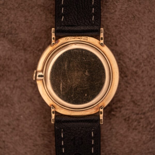 Wittnauer Ref. 2028 manual wind watch with a Cal. 11BG2 movement, white dial, gold indexes, visible case back scratches, black leather strap, shown on a brown textured surface.