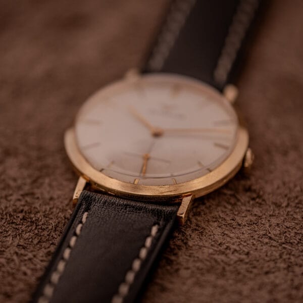 The Wittnauer Ref. 2028 Manual Wind Cal. 11BG2 with a white dial and gold indexes sits elegantly on a brown textured surface.