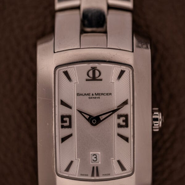 Close-up of a Baume Mercier Hampton 65511 Quartz Stainless Steel wristwatch, showing the time at 8:24 with a date window displaying 3.