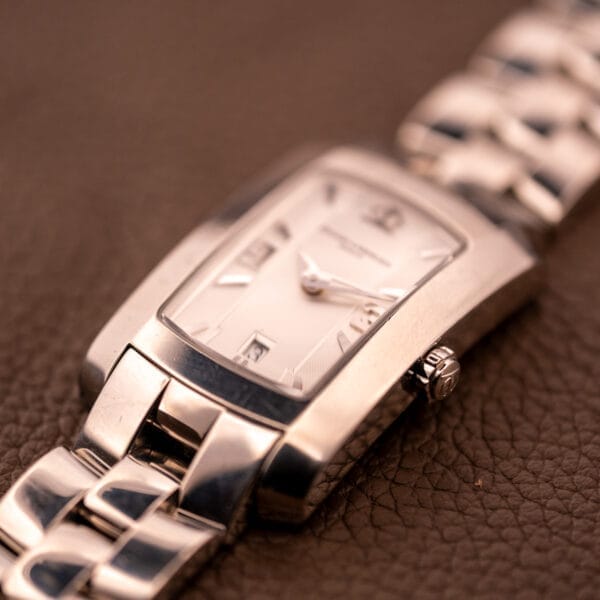 A close-up of the Baume Mercier Hampton 65511 Quartz Stainless Steel wristwatch with a rectangular face, displayed on a brown textured surface.