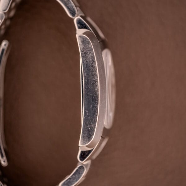 Close-up of a scratched Baume Mercier Hampton 65511 Quartz Stainless Steel watch bracelet set against a brown textured background.