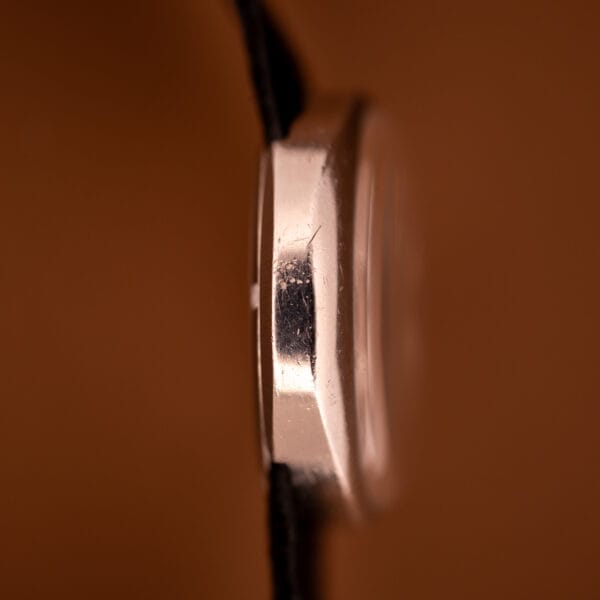 Close-up side view of a scratched silver Omega Automatic Geneve Dynamic Ref. 166.107 Cal. 1421 watch case, set against a brown background.