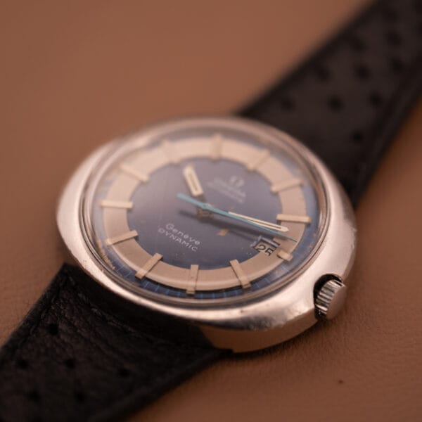 Close-up of an Omega Automatic Geneve Dynamic Ref. 166.107 Cal. 1421 wristwatch with a black strap on a beige surface.