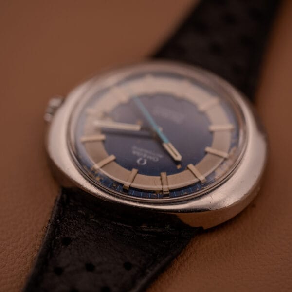 Close-up of an Omega Automatic Geneve Dynamic Ref. 166.107 Cal. 1421 watch with a black leather strap displayed on a brown surface.