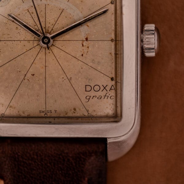 Close-up of a vintage Doxa Graphic Ref. 11728-4 featuring a stainless steel square case, patina on the dial, visible hands, and a brown leather strap.