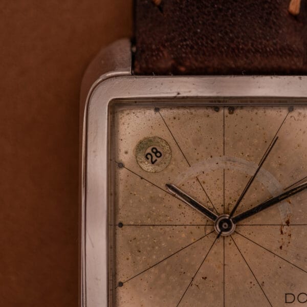 Close-up of a vintage Doxa Graphic Ref. 11728-4 with a worn face, square stainless steel case, date display at “28,” and paired with a brown leather strap.
