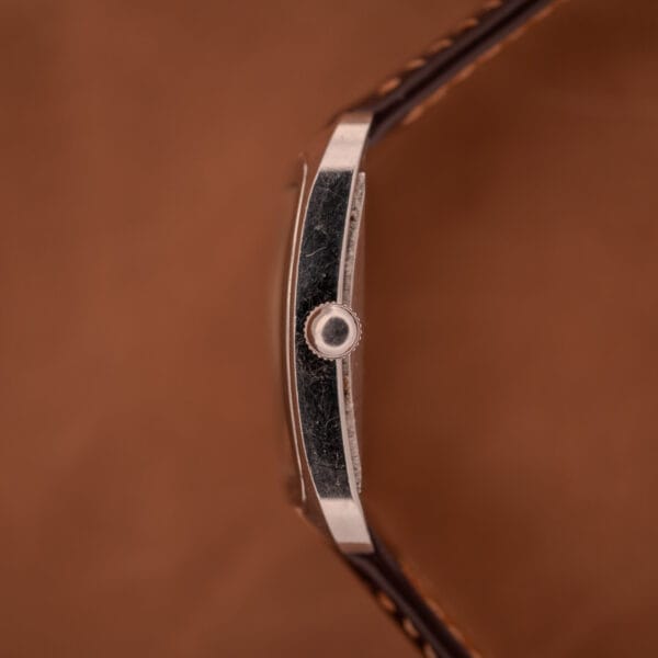 Side view of the Doxa Graphic Ref. 11728-4, featuring a stainless steel square case, brown leather strap, and visible crown, set against a brown background.