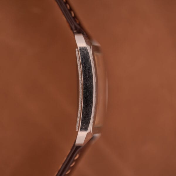 Close-up side view of a Doxa Graphic Ref. 11728-4 with a stainless steel square case and brown leather strap, set against a brown background.