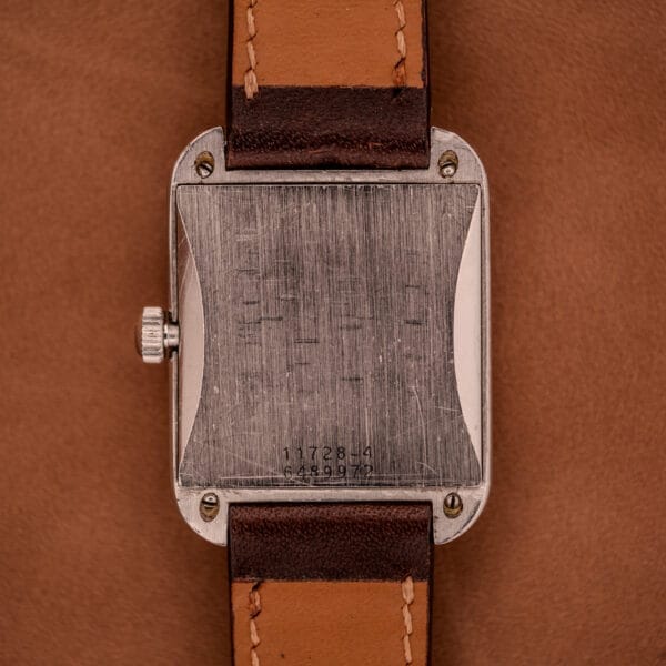 A close-up of the Doxa Graphic Ref. 11728-4 wristwatch with a stainless steel square case and leather strap, resting on a brown surface.