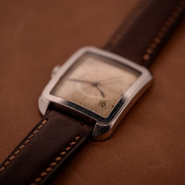 The Doxa Graphic Ref. 11728-4, featuring a stainless steel square case and brown leather strap, rests elegantly on a matching leather surface.