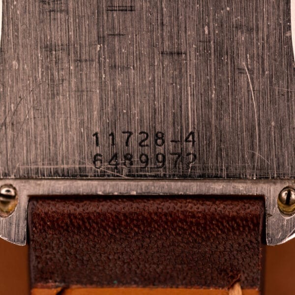 Close-up of the Doxa Graphic Ref. 11728-4 stainless steel square case watch back with engraved numbers, set above a brown leather strap, highlighting its classic design.