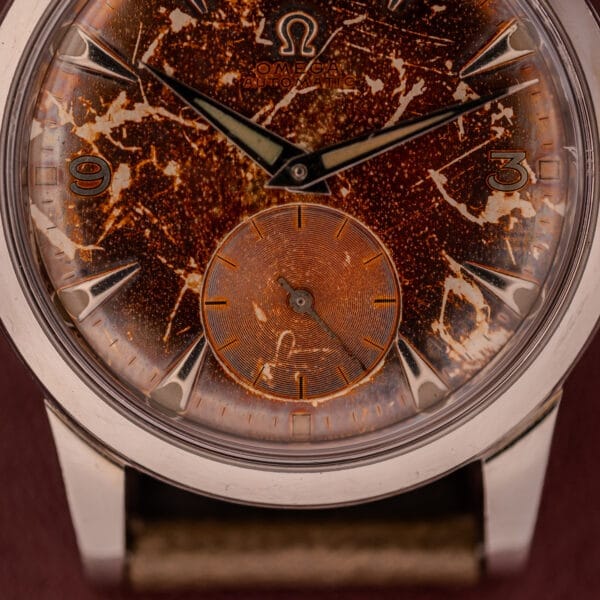 A close-up of the Omega Automatic 2491 "Pre-Seamaster" with a heavily patinated, speckled brown Tropical Dial and silver case, featuring the Cal. 28.10 RA movement.