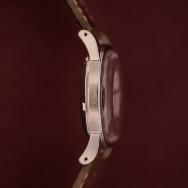 Close-up side view of the Omega Automatic 2491 "Pre-Seamaster" Tropical Dial Cal. 28.10 RA with a brown strap and metallic case, set against a maroon background.