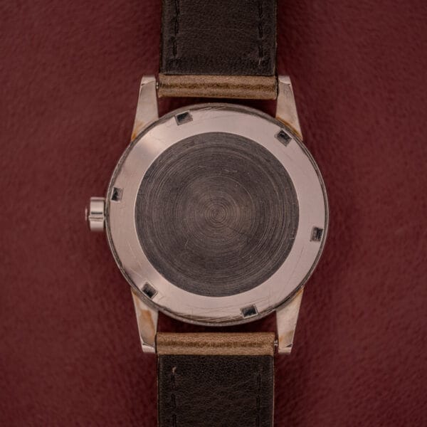 An Omega Automatic 2491 "Pre-Seamaster" Tropical Dial Cal. 28.10 RA wristwatch with a plain case back and brown leather strap sits on a burgundy surface.