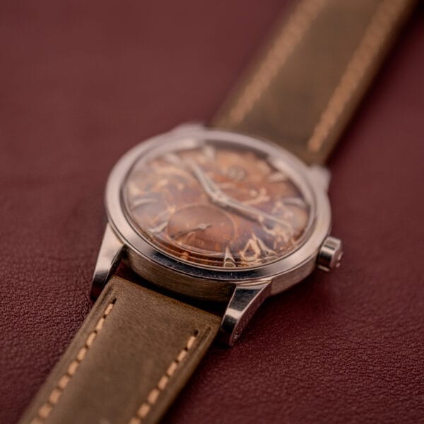 Close-up of the Omega Automatic 2491 "Pre-Seamaster" with a Tropical Dial, Cal. 28.10 RA, and brown leather strap on a red surface.