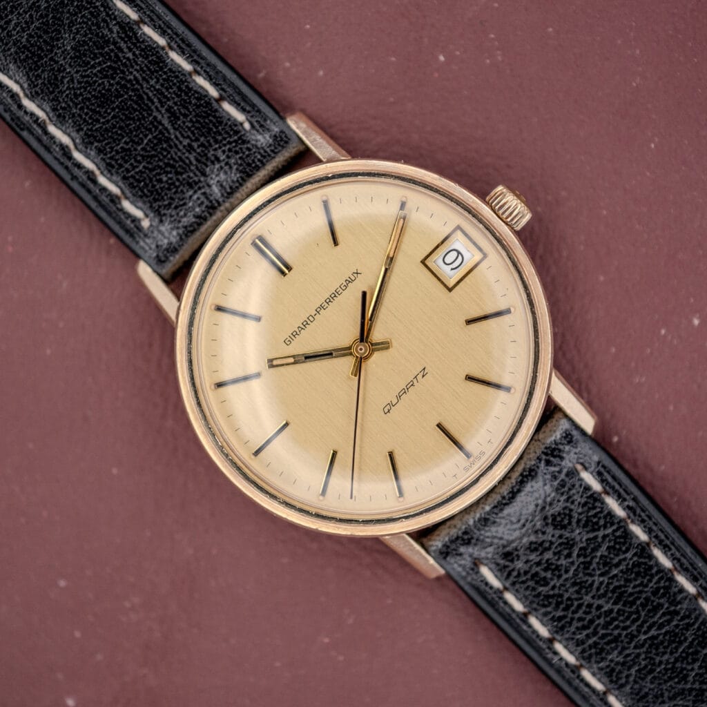 The Girard Perregaux Quartz Date 3696 features a Champagne dial, black leather strap, Cal. ETA 940 movement, and a date window, shown on a maroon background.